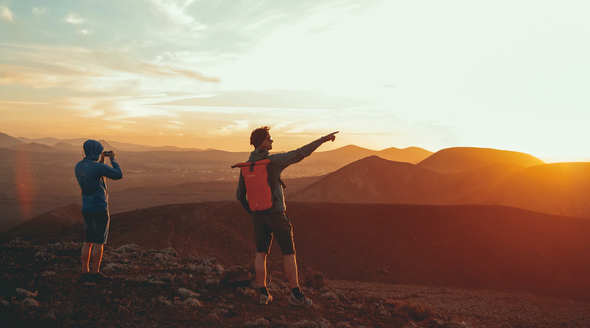 Dos amigos en lo alto de una montaña señalando el horizonte al atardecer